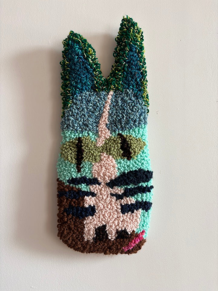 Colorful yarn art piece with green eyes and cat-like ears