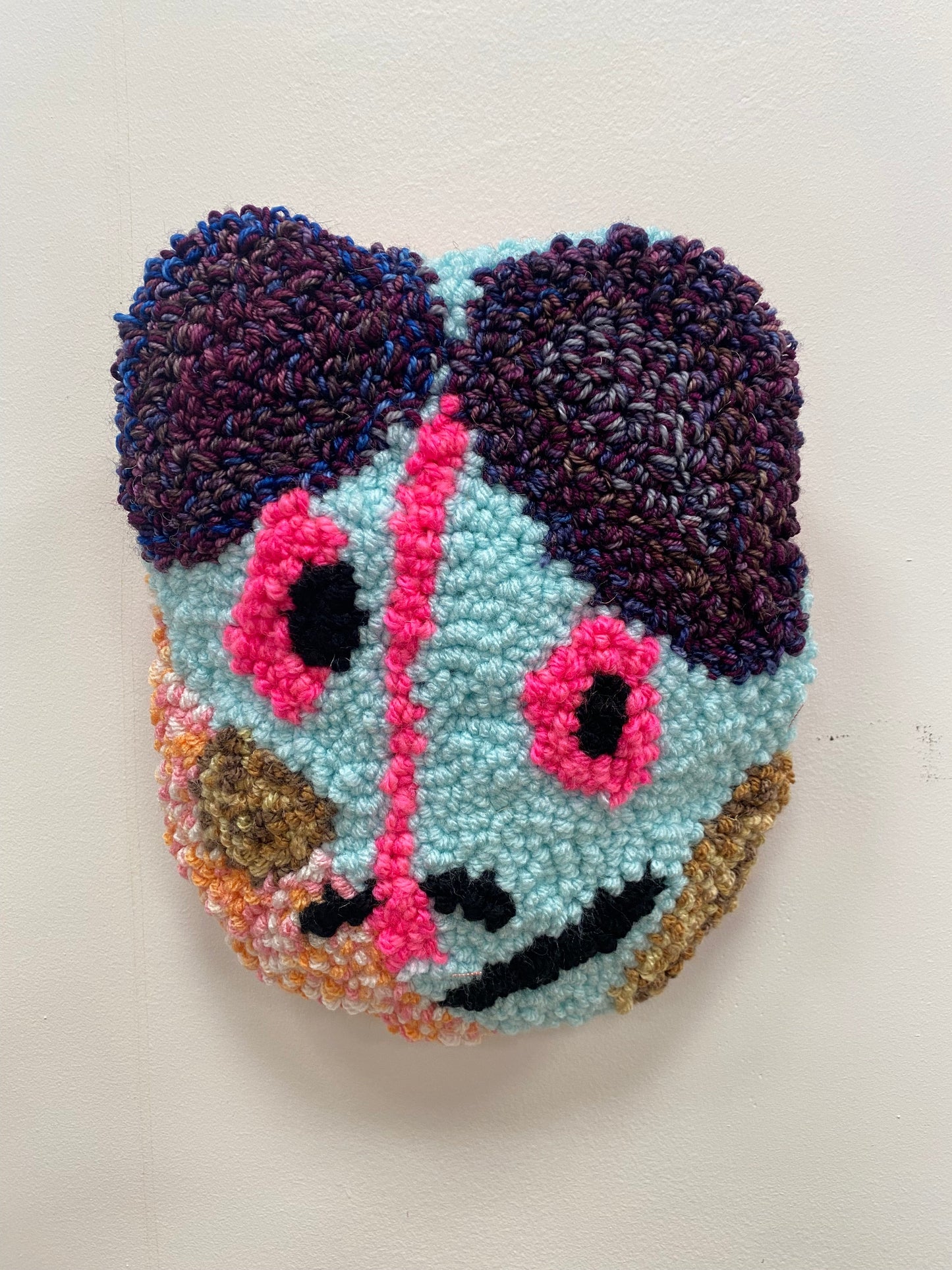 Colorful yarn art piece shaped like a face on a plain background